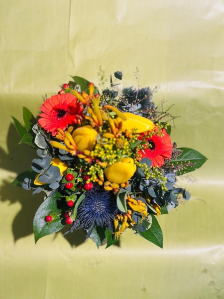 Bunter Frühlingsstrauß mit gelben Tulpen, roten Gerbera, blauen Disteln, Eukalyptus, Beeren und zarten Zweigen vor hellem Hintergrund