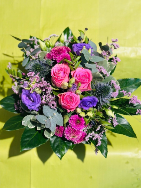 Blumenstrauß mit pinken Rosen, violettem Lisianthus, pinken Chrysanthemen, Edeldisteln und Eukalyptus auf hellem Hintergrund