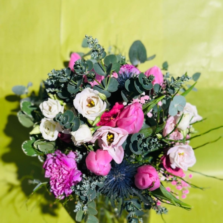 Zarter Blumenstrauß mit weißen und rosafarbenen Lisianthus, pinken Tulpen, Nelken, Edeldisteln und Eukalyptus vor hellgrünem Hintergrund