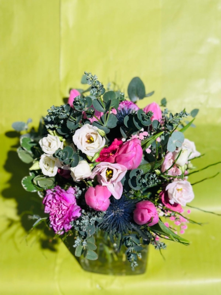 Zarter Blumenstrauß mit weißen und rosafarbenen Lisianthus, pinken Tulpen, Nelken, Edeldisteln und Eukalyptus vor hellgrünem Hintergrund